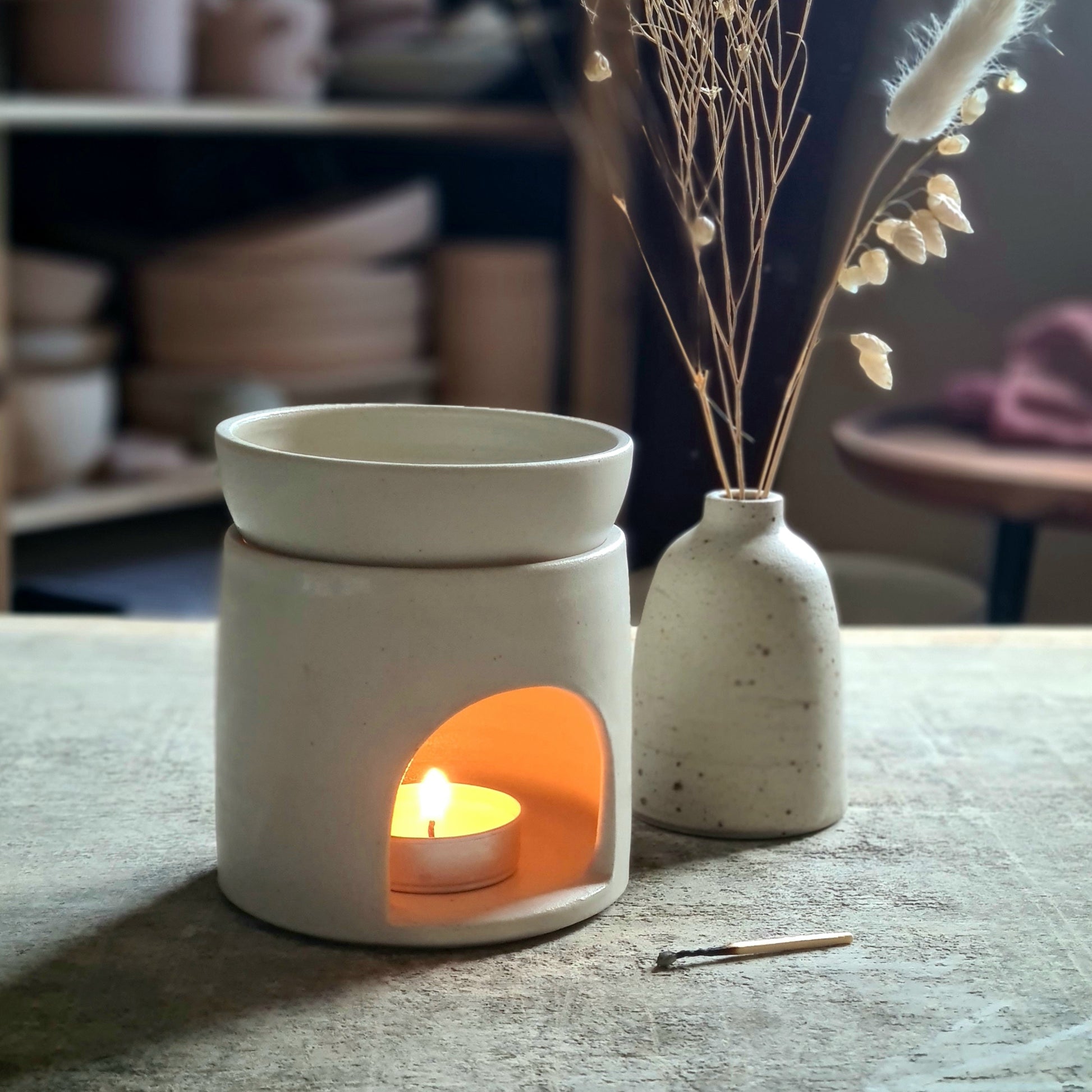Brûle-parfum artisanal en céramique blanche, bougie allumée pour diffuser des huiles essentielles.