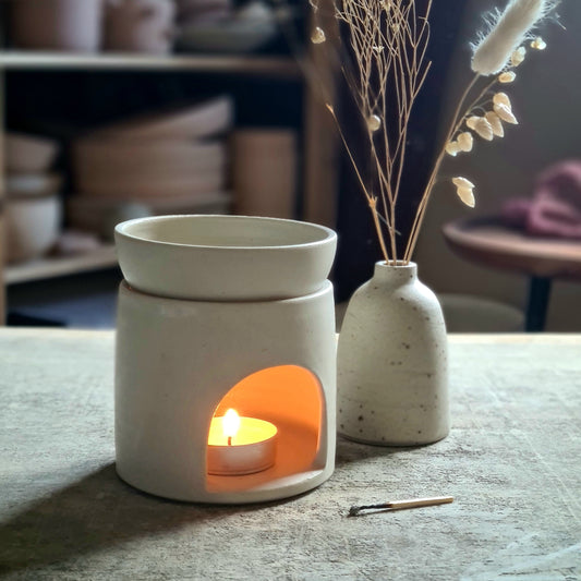 Brûle-parfum artisanal en céramique blanche, bougie allumée pour diffuser des huiles essentielles.